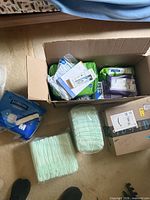 Overview of open box with assorted medical supplies including multiple packs of adult underwear, boxed small devices, nearby FitRight pack and loose briefs