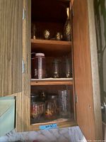 Cabinet view showing amber vase, gilt cordials, filigree tumblers, plastic bottle, maple leaf glasses, blue grape tumbler