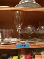 Shelf view showing clear wine glass, Pyrex measuring cup, and painted goblets