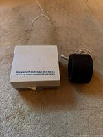 Closed Polaroid Portrait Kit box beside black winding case