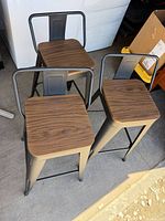 Three black metal bar stools with brown wood seats, top view