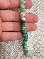 Close-up of strand showing variegated green disc beads against hand for scale