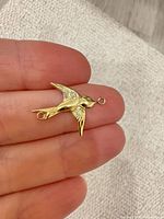Front of gold swallow connector held between fingers