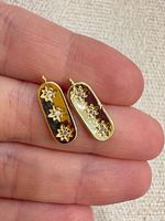 Front view of both pendants on fingertip showing stone placement and gold tone
