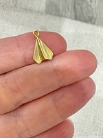 Front view of gold-tone paper airplane pendant held between fingers