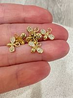 Five gold tone bee charms shown on fingertip for scale