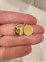 front and back of both gold tone rose coin pendants held in hand