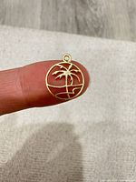 Front view of gold-tone palm tree pendant on fingertip