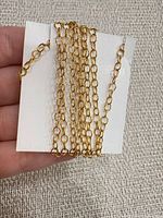 Coiled gold tone rolo link chain displayed on white card
