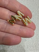 Close-up of three M charms on fingertip showing gold-tone finish