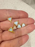 Six gold-tone triangle opal charm pendants on fingertip for scale