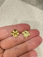 Pair of gold paw print pendants on fingertip showing scale