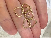 six small gold-tone twisted rope heart charms on fingertip