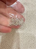 Close-up of small plastic bag containing silver jump rings held between fingers