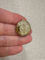 Front view of ornate gold-tone round locket held in hand