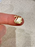 Front view of gold-plated swan charm on fingertip showing size and design