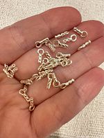 Hand holding multiple sterling silver cord end crimps to show quantity and scale.