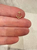 Front view of gold-tone anchor pendant on fingertip