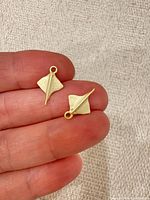 Front view of both matte gold-tone stingray charms on fingertip for scale