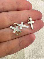Three sterling silver cross pendants on fingertip for scale