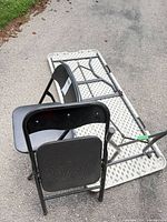 Table folded upside down showing HDPE top pattern and steel frame; two black folding chairs leaning