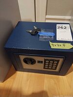 Front and top view of blue steel safe showing keypad, key lock, keys, measurement note