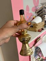 Side view of gold Library Lamp bottle with cap showing shape and finish wear
