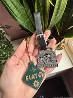 Both keychains in hand showing Caterpillar metal fob and Fiat green tag