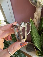 Front and side view of ornate silver-plated tea glass holder showing design and patina