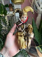 Front view of porcelain jester doll in gold and black outfit