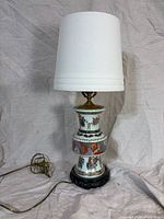Full view of lamp showing porcelain body, wooden base, brass hardware, shade, cord