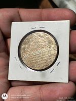 Obverse of brass token in 2x2 holder showing park logo and wonder dollar text