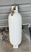 Full view of white vinyl fender lying on concrete, rope visible