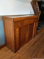 Front view of medium brown Art Deco sideboard showing two doors, one drawer, brass knobs, overall form