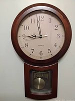 Front view of wooden quartz wall clock showing dial and lower Regulator window