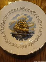 Front view showing sailing ship artwork, gold vine border, scalloped gold rim