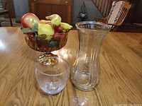 Amber pedestal fruit bowl filled with faux fruit, clear glass vase, clear tumbler on wooden table