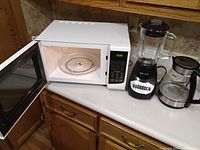 Microwave with door open showing interior turntable, blender, and kettle