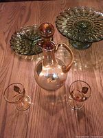 Group shot of amber decanter, two cordial glasses, and two green pedestal compote dishes