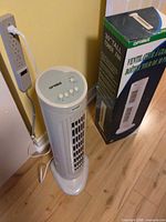 Fan plugged in beside wall showing full height and retail box