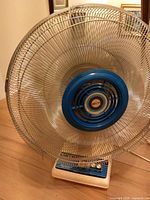Front view of fan showing blue blades, chrome grill, cream base