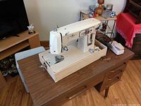 Full view of sewing machine mounted in wooden cabinet with foot pedal on tabletop