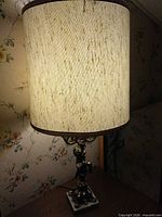 Full view of lit ornate brass cherub lamp with fabric shade