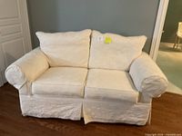 Front view of ivory/cream slipcovered loveseat showing cushions and rolled arms