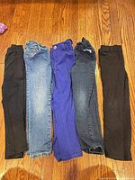 Five folded pairs of children's jeans in various colors laid on hardwood floor
