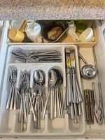 Drawer organizer holding stainless flatware, knives, straws, sink strainer, measuring cups, ceramic cups and dish