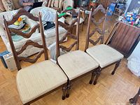Front view of three matching dark wood ladder-back dining chairs with beige upholstered seats
