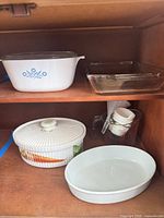 Shelf view showing cornflower casserole, glass baking dish, vegetable motif casserole, measuring jug, cups, white oval baker