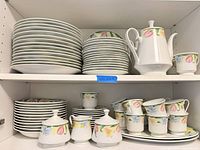 Cabinet shelves showing full dinnerware set including plates, bowls, cups, teapot and sugar bowls