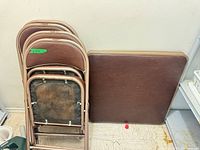 Stacked four folding chairs and folded table top leaning against wall